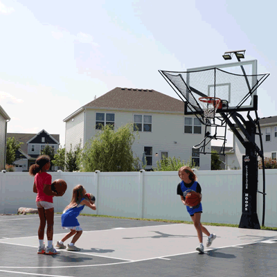 Three players shooting on Dr. Dish IC3 Basketball Shot Trainer in backyard